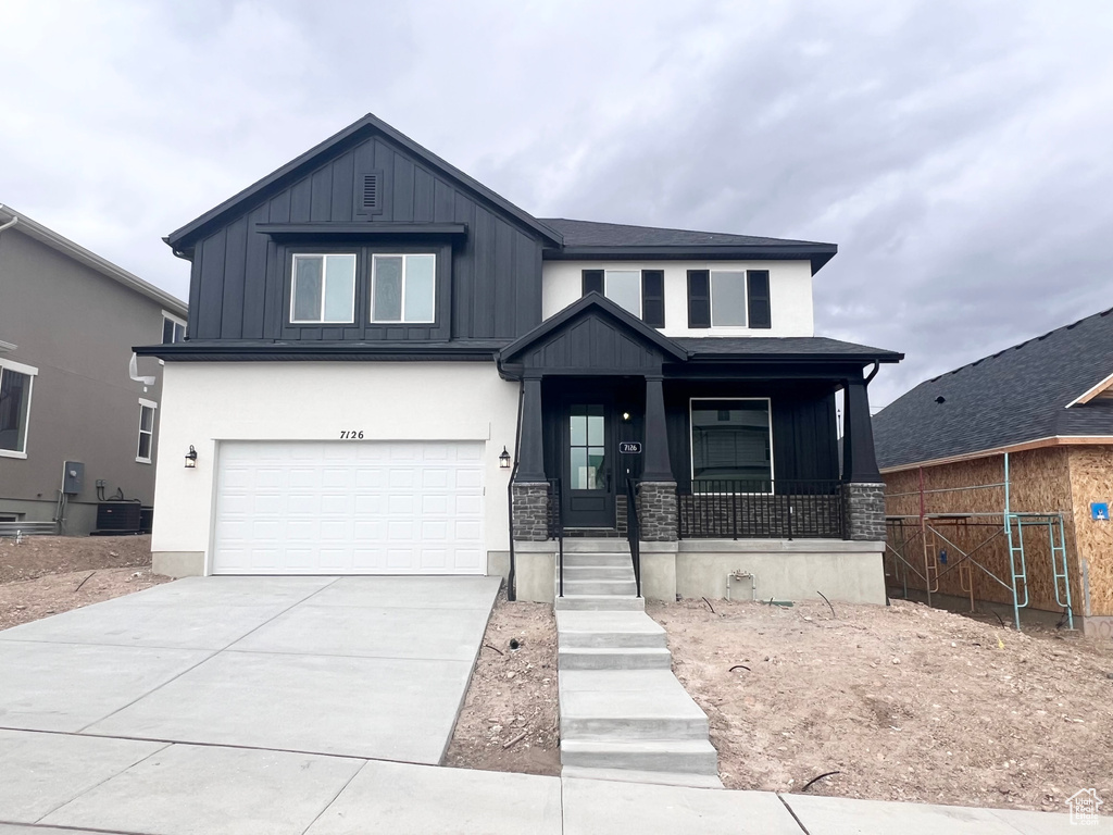 View of front of property with a porch, board and batten siding, an attached garage, stone siding, and concrete driveway