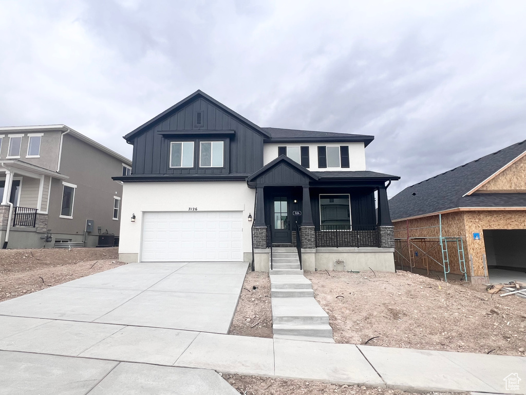 View of front of home featuring an attached garage, board and batten siding, concrete driveway, a porch, and stone siding