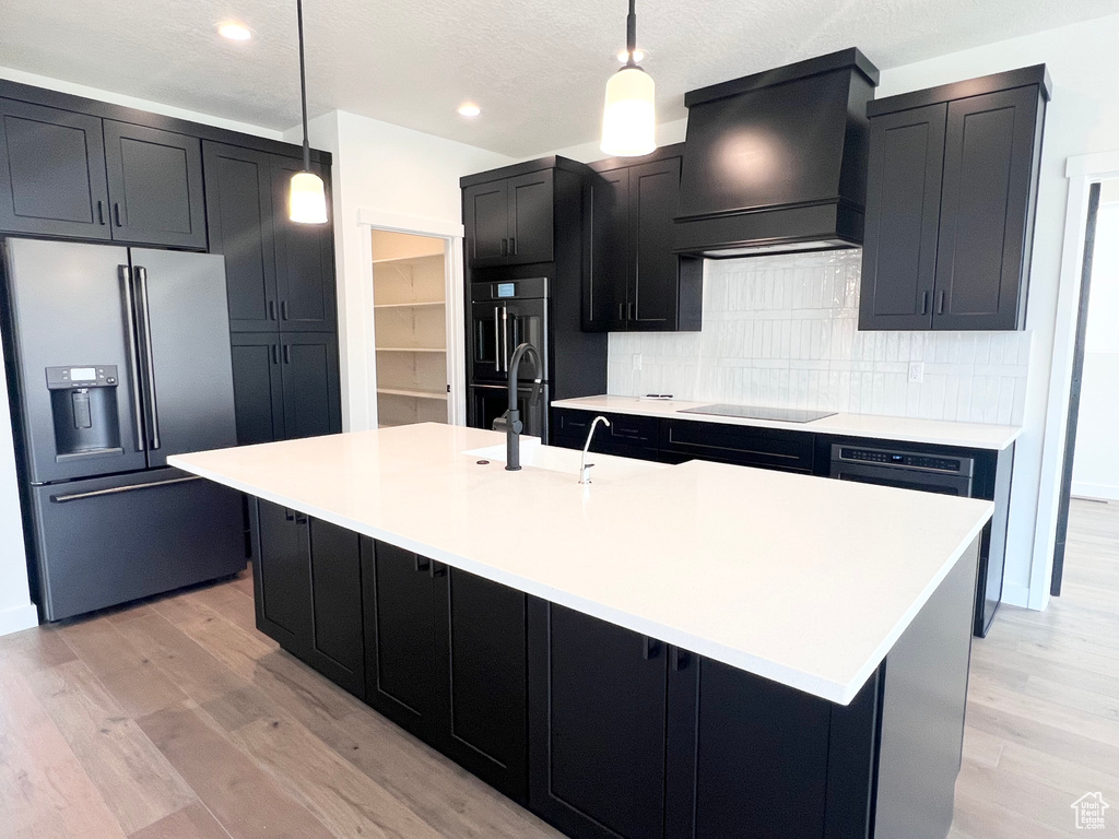 Kitchen featuring high end refrigerator, custom range hood, dark cabinets, black electric cooktop, and decorative backsplash