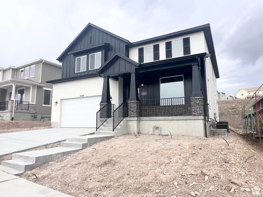 Craftsman inspired home featuring board and batten siding, a garage, driveway, covered porch, and stone siding