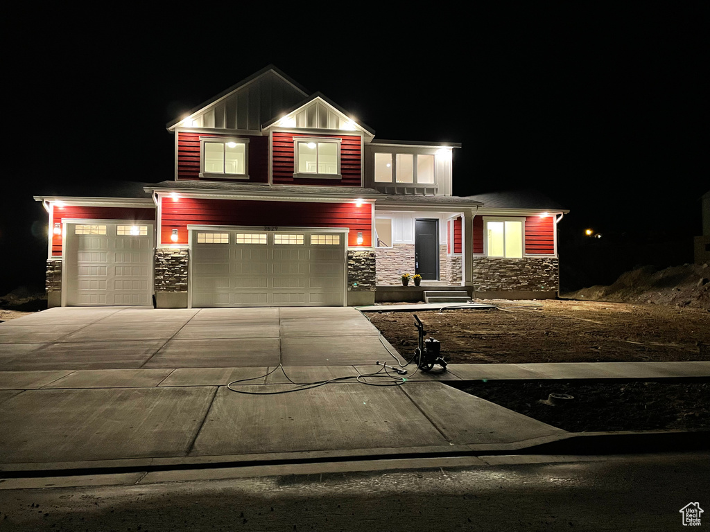 View of front facade with stone siding, driveway, board and batten siding, and a garage