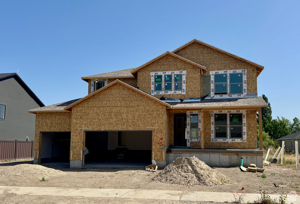Property under construction with dirt driveway, an attached garage, and a shingled roof