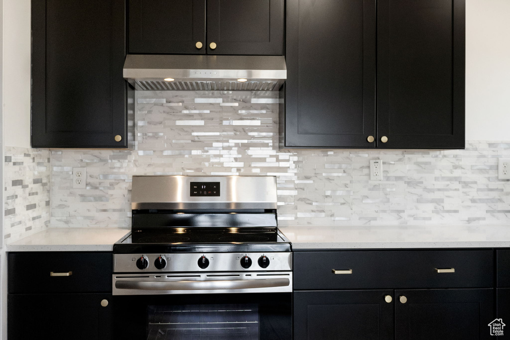 Kitchen featuring electric range, ventilation hood, decorative backsplash, and light countertops