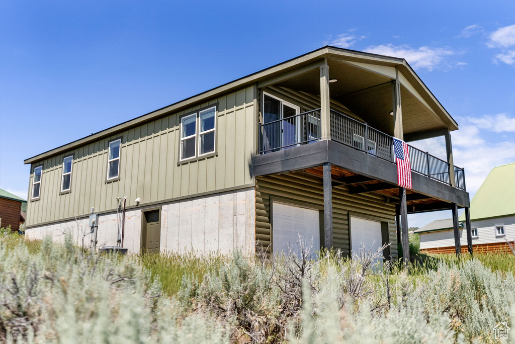 Rear view of property featuring board and batten siding, an attached garage, and a balcony