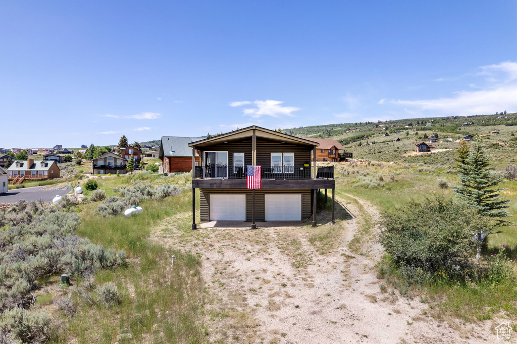 View of front facade with dirt driveway, an attached garage, a wooden deck, and log veneer siding