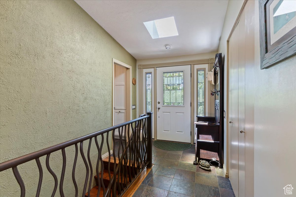 Foyer entrance with a textured wall, stone tile flooring, a skylight, and vaulted ceiling