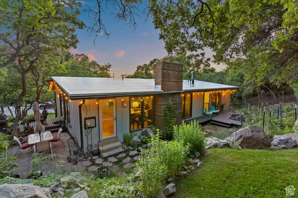 Back of property with a chimney, a deck, a patio, board and batten siding, and a lawn