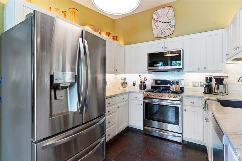 Kitchen with stainless steel appliances, tasteful backsplash, white cabinetry, and dark stone finish floors