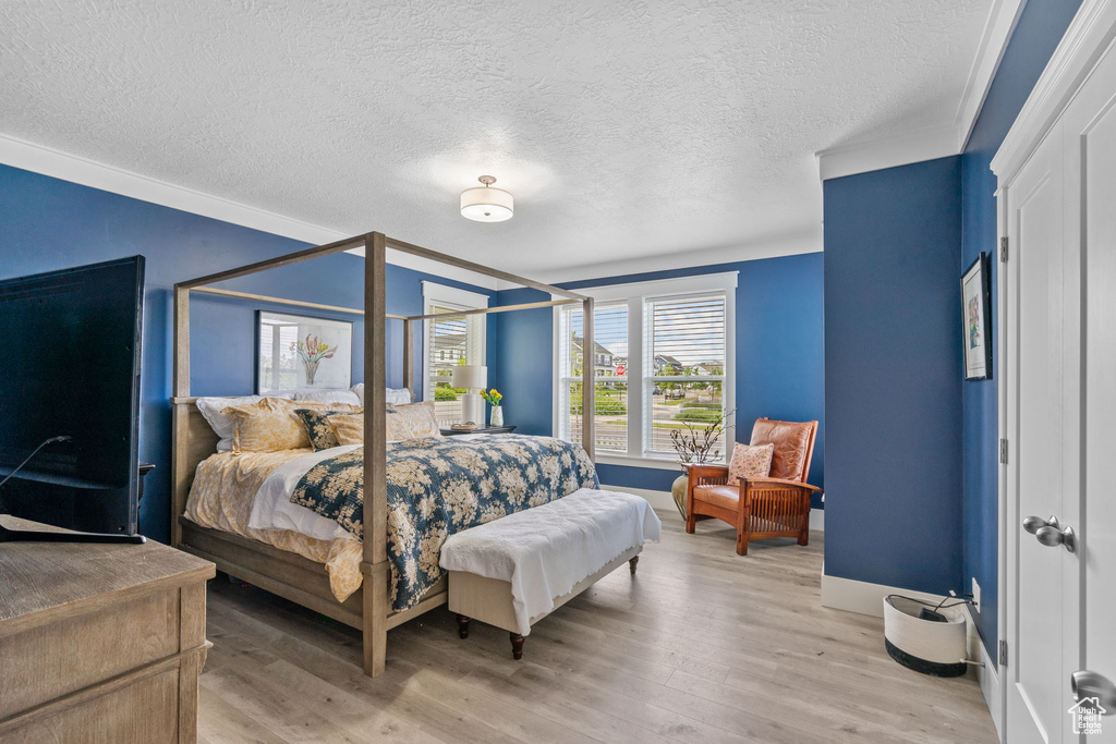 Bedroom featuring light wood-type flooring, crown molding, and a textured ceiling
