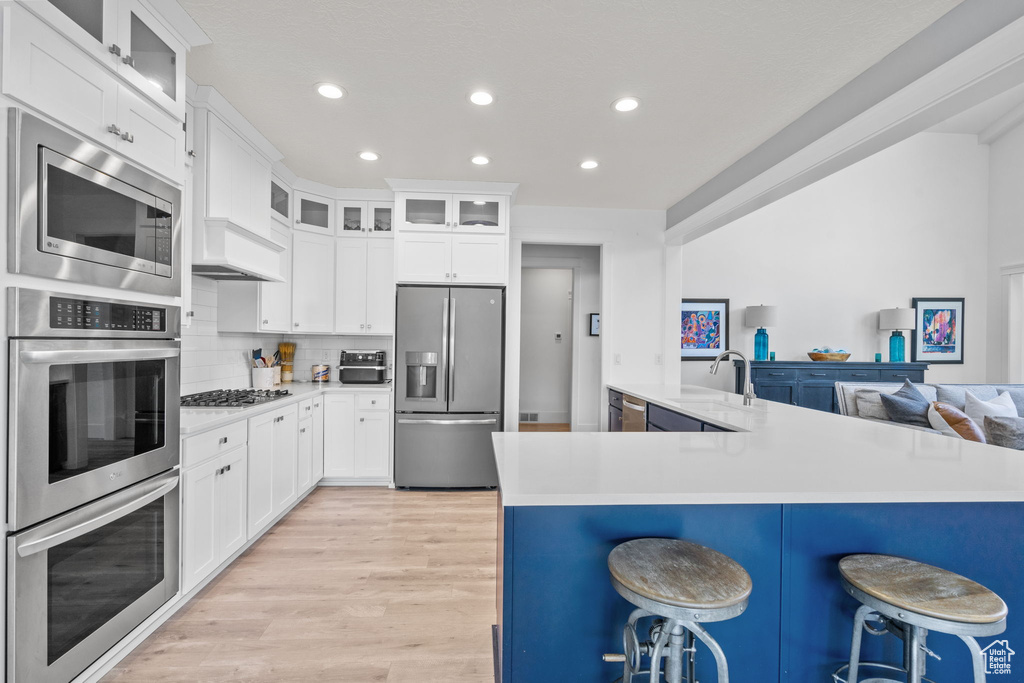 Kitchen featuring stainless steel appliances, a breakfast bar area, light wood-style floors, recessed lighting, and light countertops