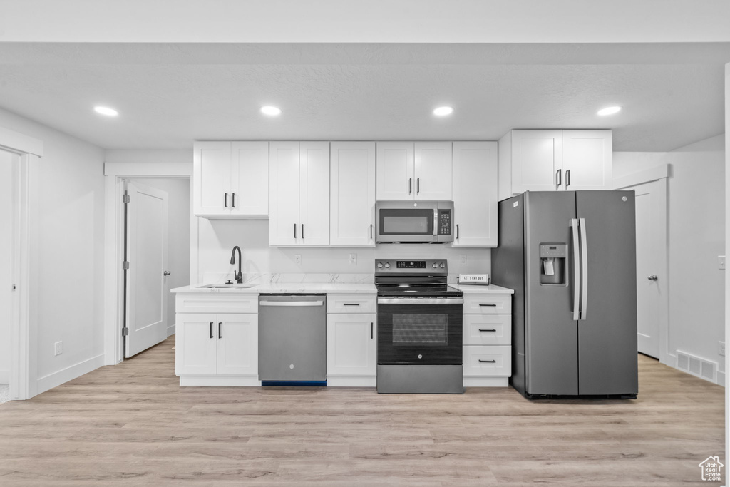 Kitchen featuring stainless steel appliances, white cabinetry, light countertops, light wood-style floors, and recessed lighting
