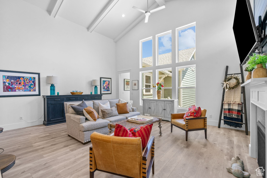 Living area with a fireplace, high vaulted ceiling, beam ceiling, light wood-type flooring, and a ceiling fan