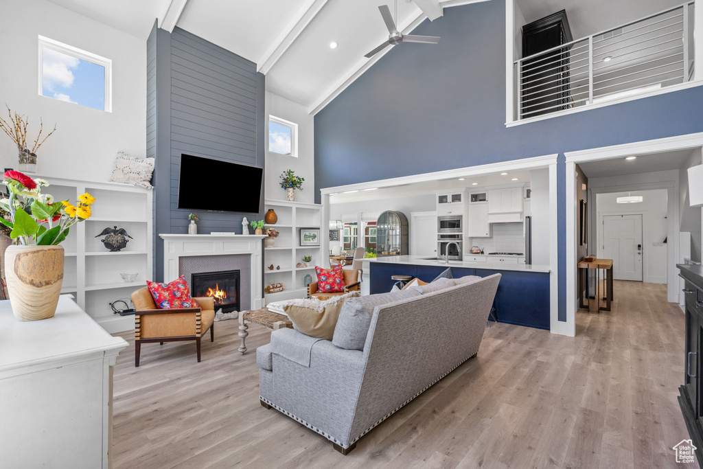 Living area featuring high vaulted ceiling, a ceiling fan, a fireplace, beamed ceiling, and light wood-type flooring