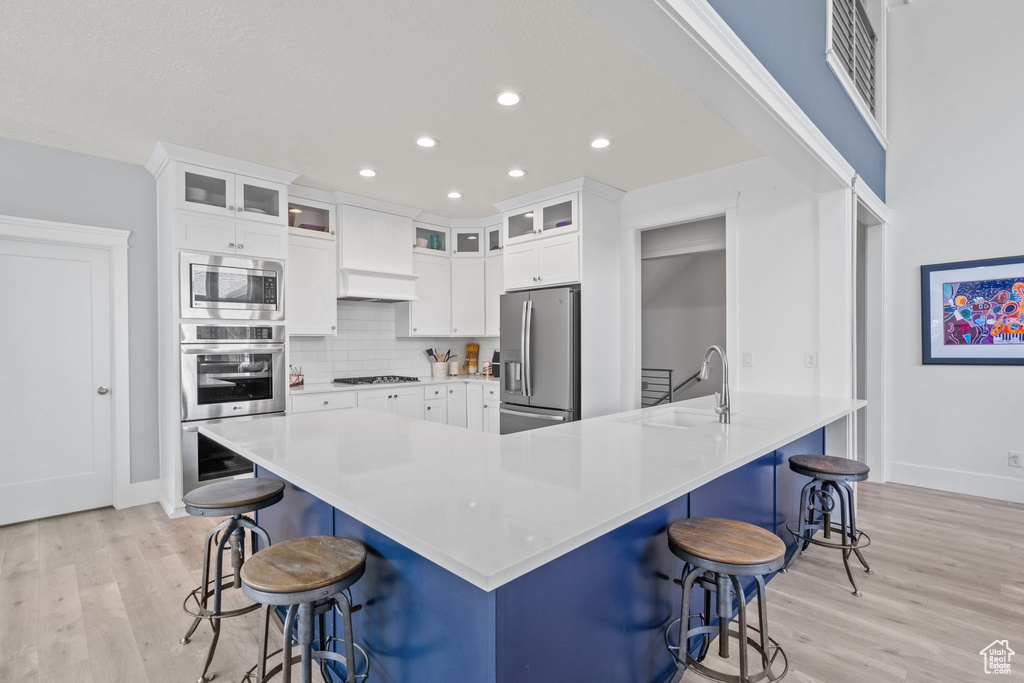 Kitchen featuring stainless steel appliances, light wood finished floors, recessed lighting, white cabinets, and tasteful backsplash