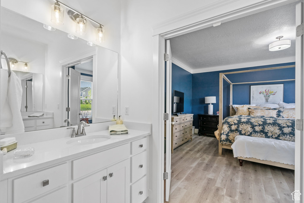 Bathroom featuring ensuite bathroom, vanity, wood finished floors, a textured ceiling, and crown molding