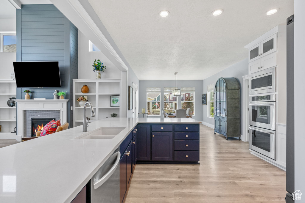 Kitchen with stainless steel appliances, open floor plan, light wood finished floors, light countertops, and a glass covered fireplace