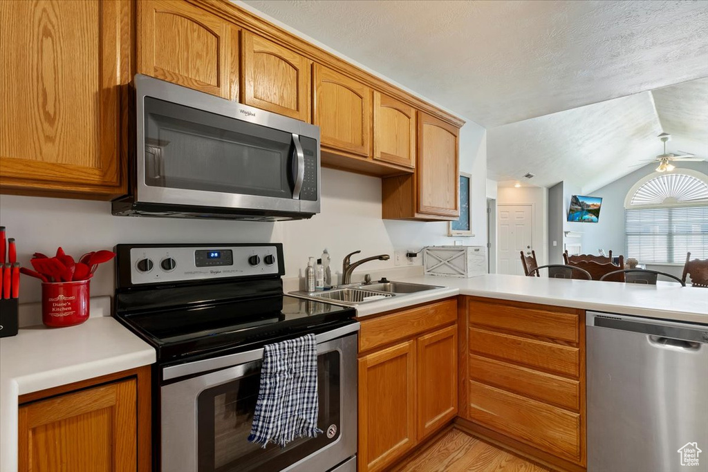 Kitchen with stainless steel appliances, light countertops, a ceiling fan, light wood finished floors, and lofted ceiling