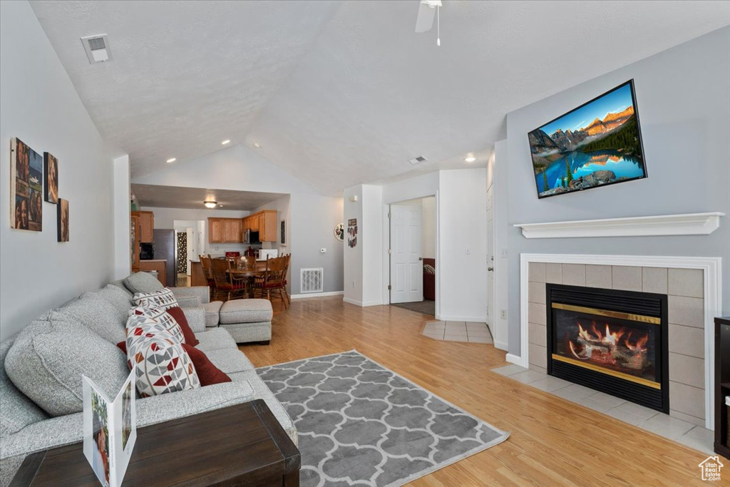 Living area with light wood finished floors, a fireplace, lofted ceiling, recessed lighting, and a ceiling fan