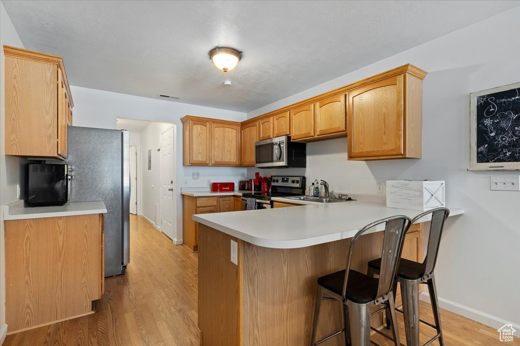 Kitchen with appliances with stainless steel finishes, a peninsula, a breakfast bar area, light wood-style flooring, and light countertops