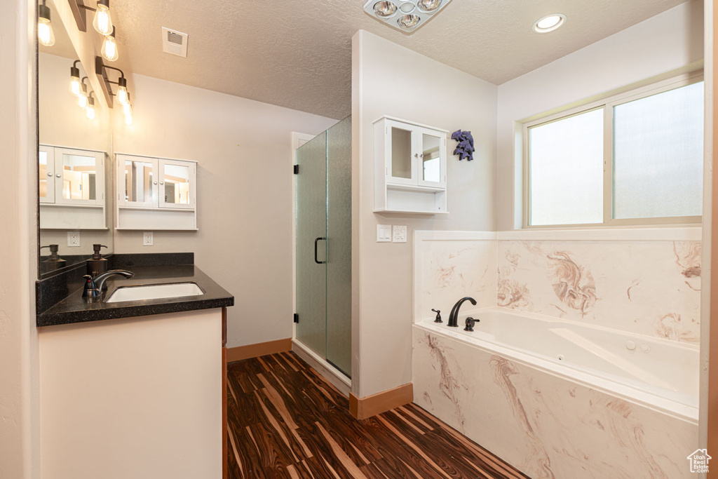 Full bath featuring a stall shower, a garden tub, wood finished floors, double vanity, and a textured ceiling