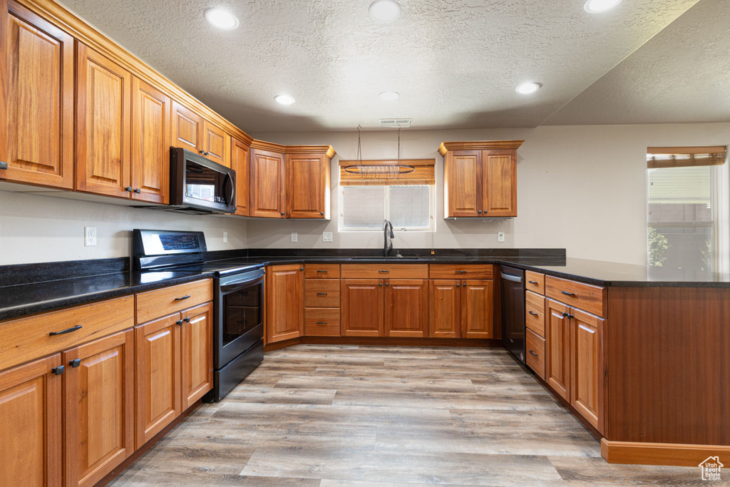 Kitchen featuring stainless steel range with electric stovetop, black microwave, a textured ceiling, a peninsula, and plenty of natural light