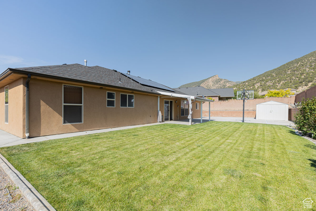 Rear view of house with a storage shed, solar panels, a patio, a fenced backyard, and a mountain view