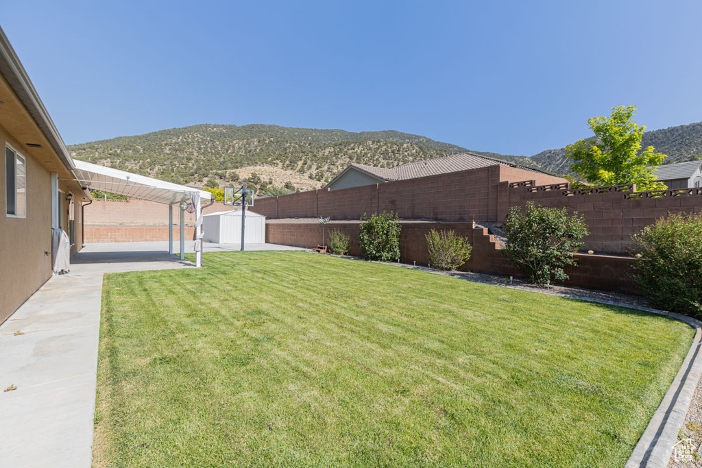 Fenced backyard featuring a mountain view, a patio, and a storage shed