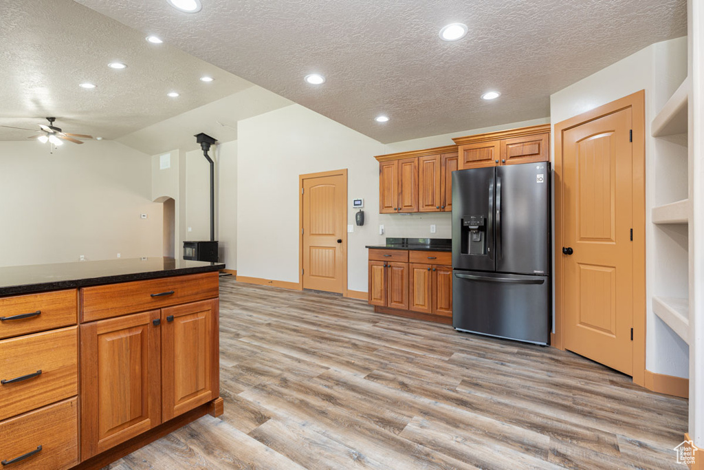 Kitchen with black fridge, a textured ceiling, lofted ceiling, ceiling fan, and light wood-type flooring