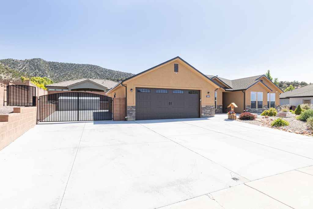 Ranch-style house featuring stone siding, a gate, stucco siding, and an attached garage