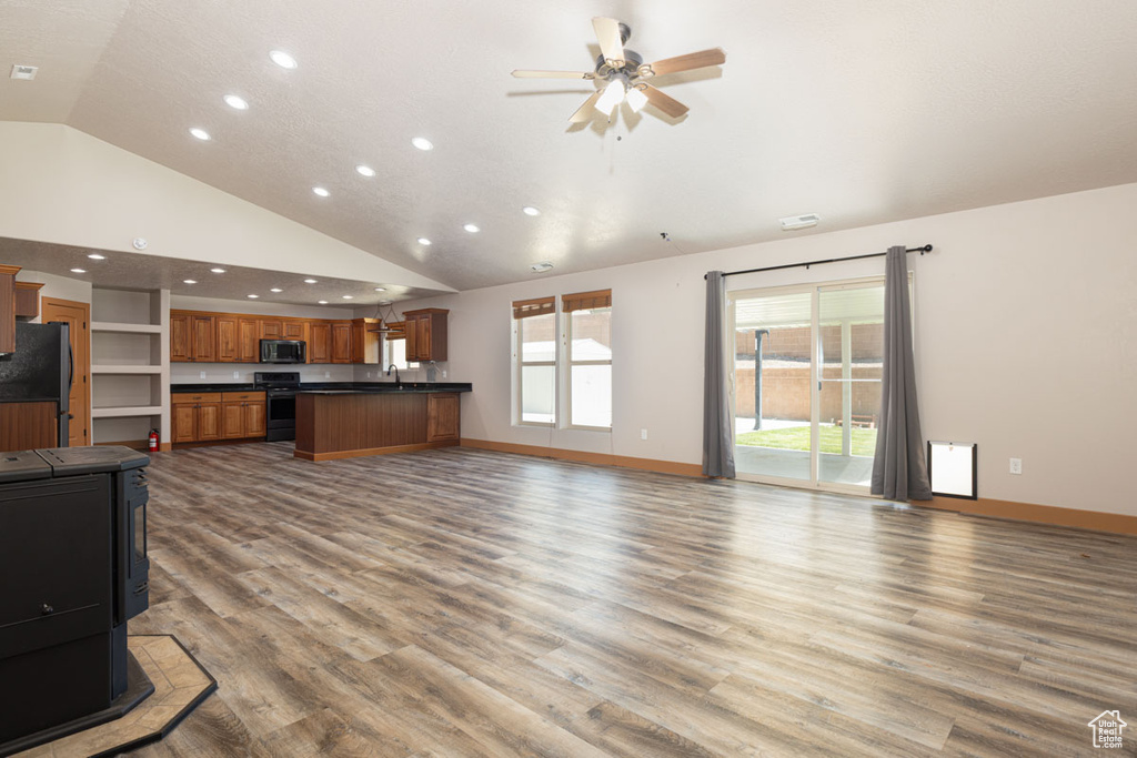 Unfurnished living room featuring recessed lighting, a ceiling fan, wood finished floors, a wood stove, and high vaulted ceiling