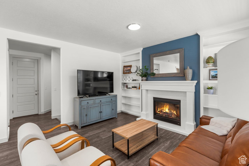 Living area with built in features, a glass covered fireplace, and dark wood-style flooring