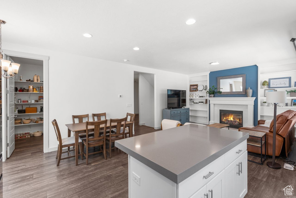 Kitchen featuring dark wood-type flooring, a center island, a glass covered fireplace, white cabinets, and recessed lighting
