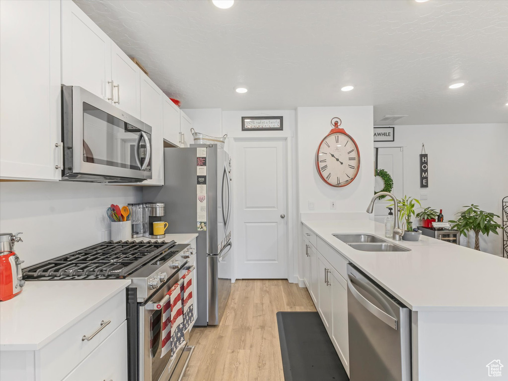 Kitchen with stainless steel appliances, light wood-type flooring, a peninsula, white cabinetry, and recessed lighting