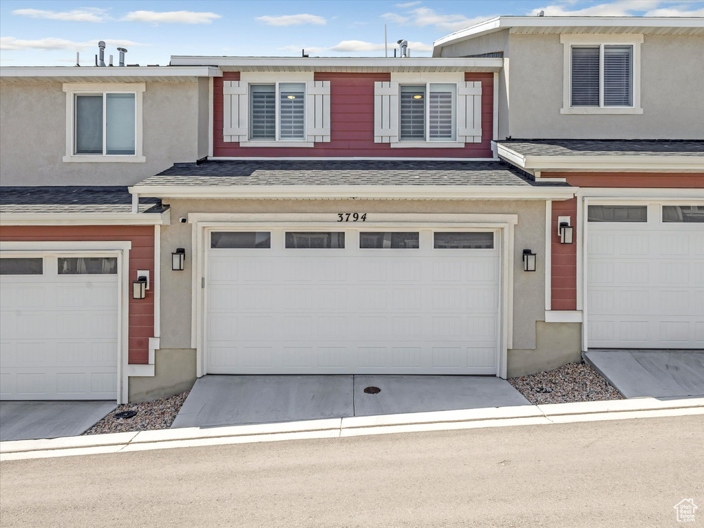 Townhome / multi-family property featuring an attached garage, stucco siding, driveway, and roof with shingles
