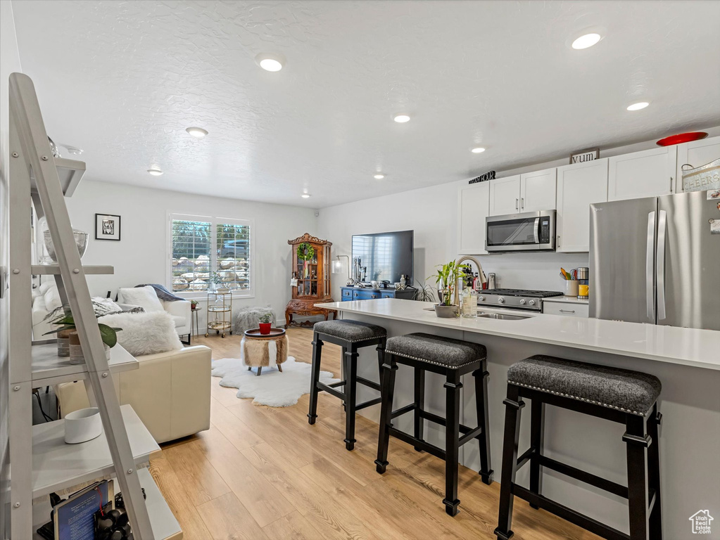 Kitchen featuring appliances with stainless steel finishes, open floor plan, light wood-type flooring, a breakfast bar, and recessed lighting