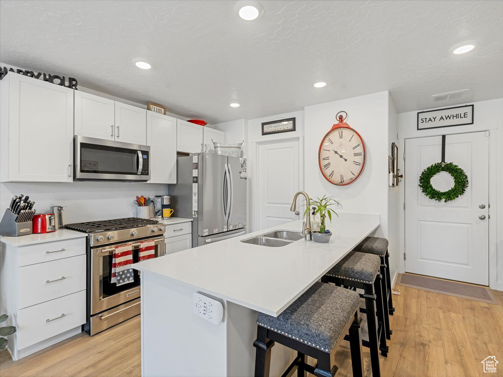 Kitchen with appliances with stainless steel finishes, a kitchen breakfast bar, light wood-style flooring, light countertops, and recessed lighting