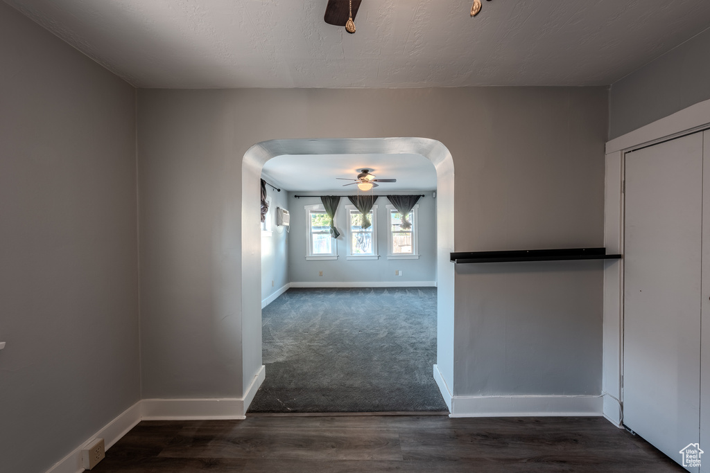 Empty room with arched walkways, ceiling fan, and dark wood-style floors