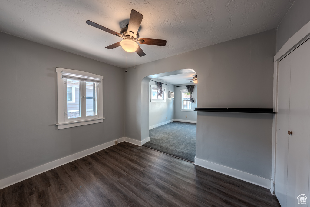 Empty room with a ceiling fan, arched walkways, dark wood-type flooring, and a textured ceiling