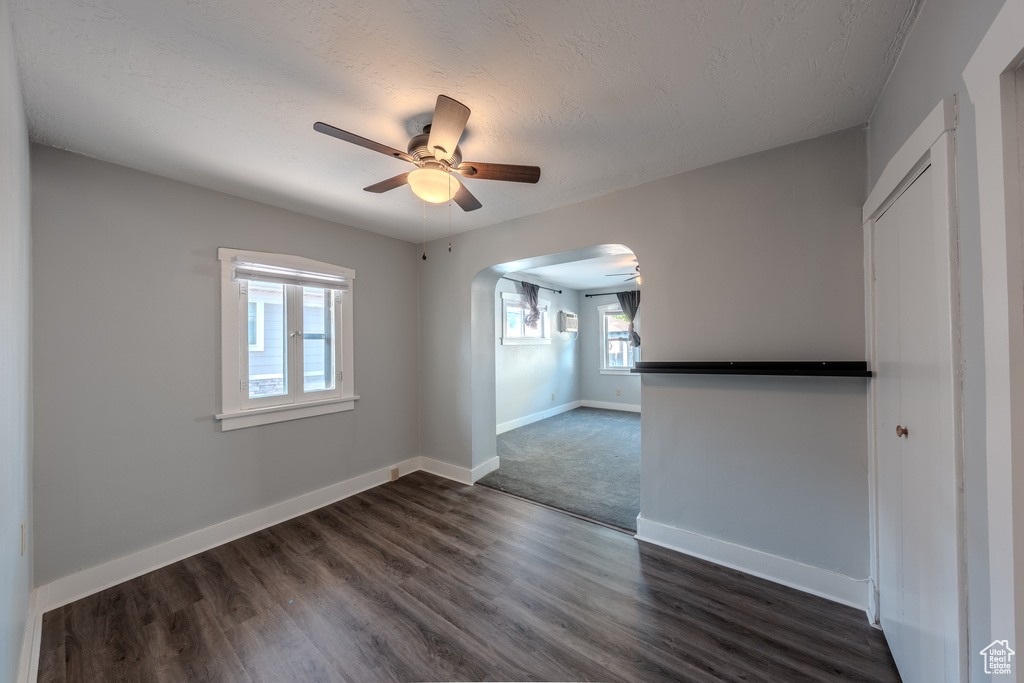 Empty room featuring ceiling fan, arched walkways, and dark wood-style floors