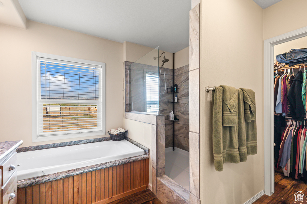 Bathroom with wood finished floors, a walk in shower, a spacious closet, a garden tub, and vanity
