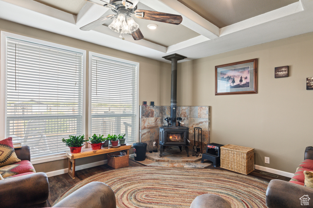 Living room with a wood stove, ceiling fan, coffered ceiling, wood finished floors, and beam ceiling