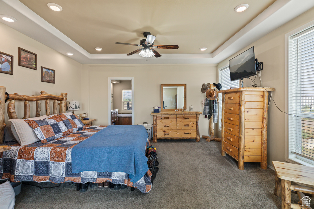 Carpeted bedroom with a raised ceiling, recessed lighting, connected bathroom, and a ceiling fan
