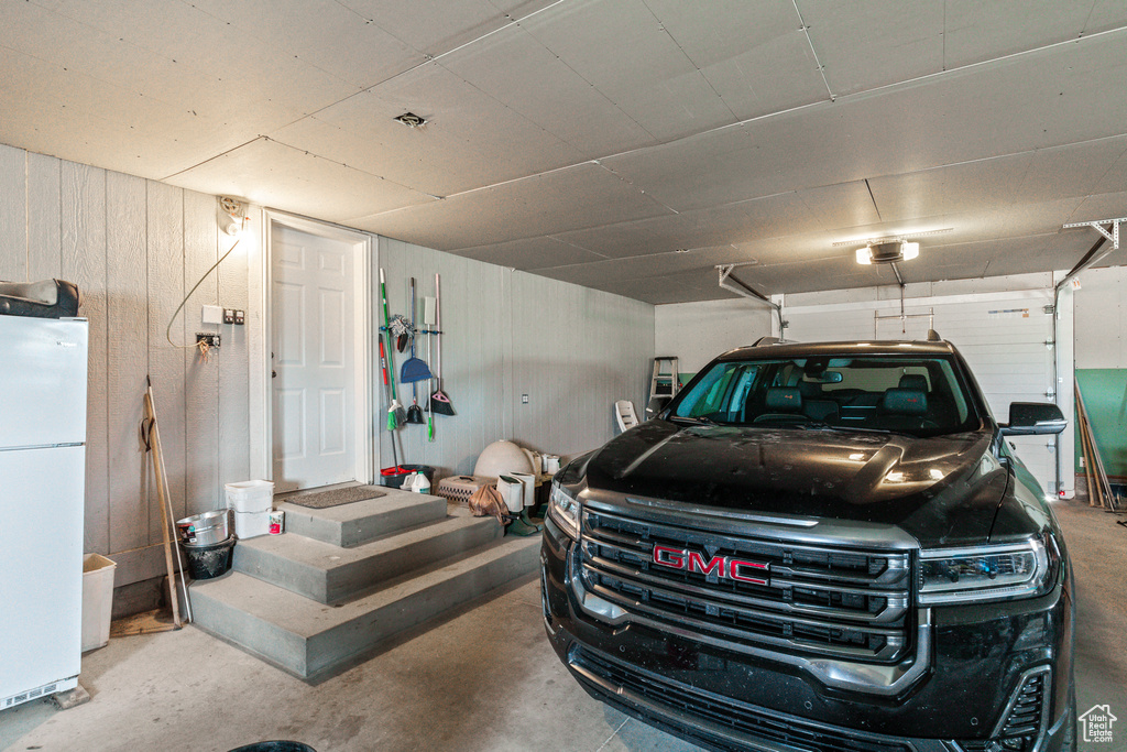 Garage featuring freestanding refrigerator, wooden walls, and a garage door opener