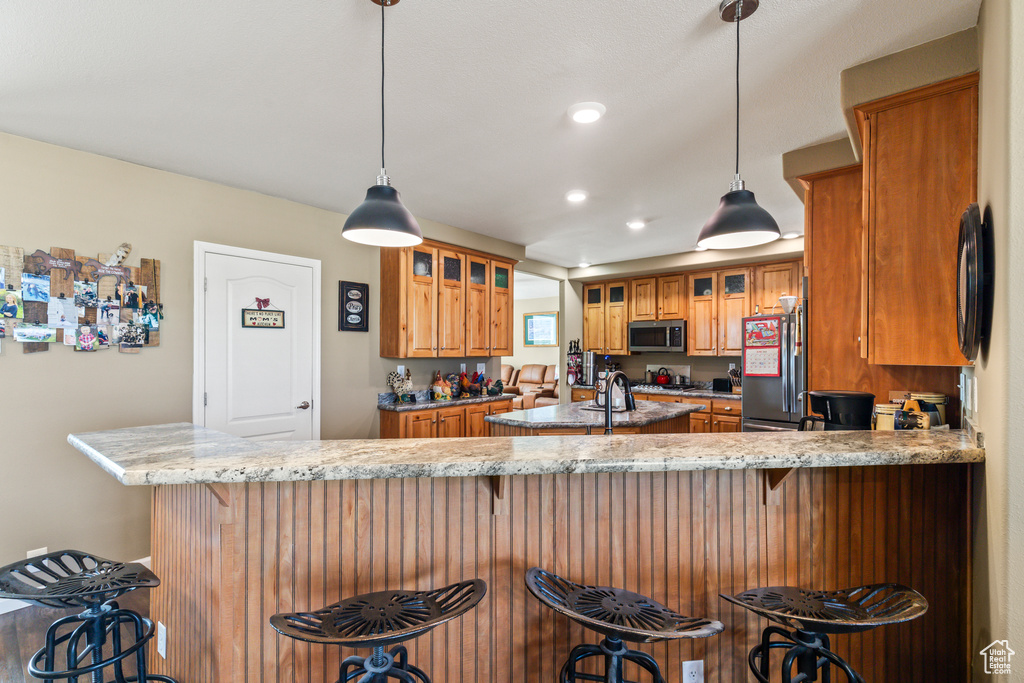 Kitchen with stainless steel microwave, fridge, brown cabinetry, a peninsula, and recessed lighting