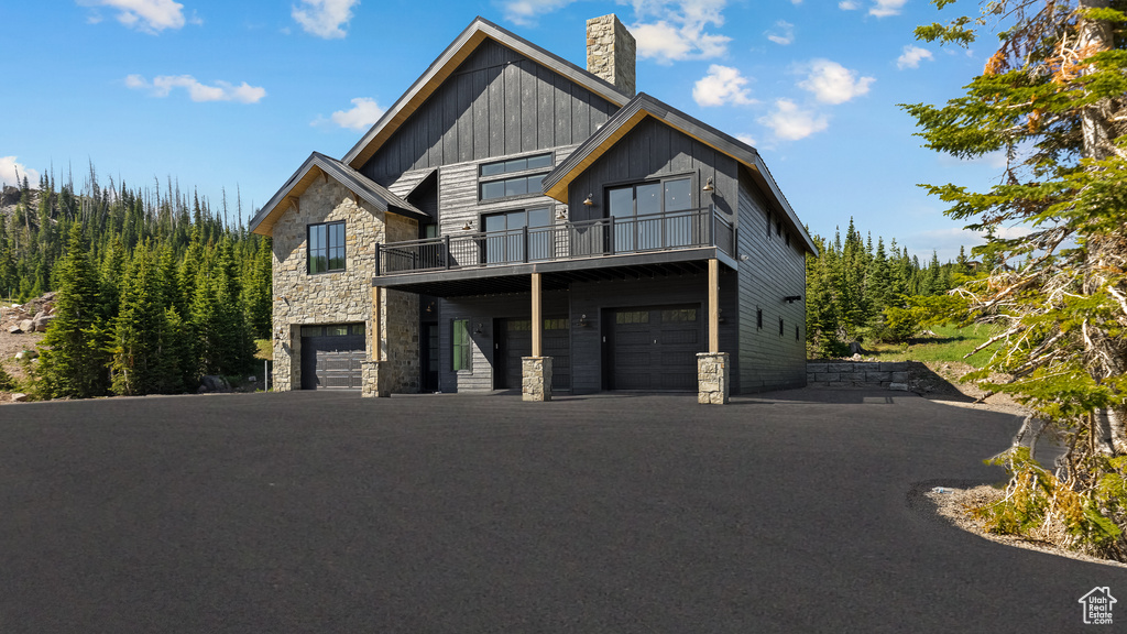 View of front of property with stone siding, a garage, a chimney, board and batten siding, and a balcony