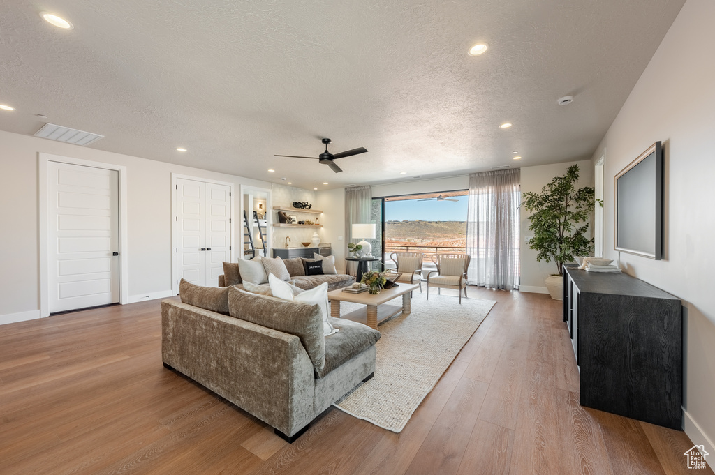 Living area with a textured ceiling, wood finished floors, recessed lighting, and ceiling fan