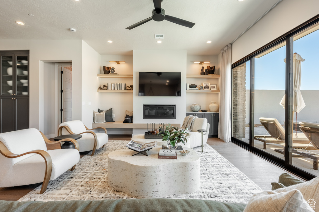 Living area featuring wood finished floors, a ceiling fan, a glass covered fireplace, recessed lighting, and built in features