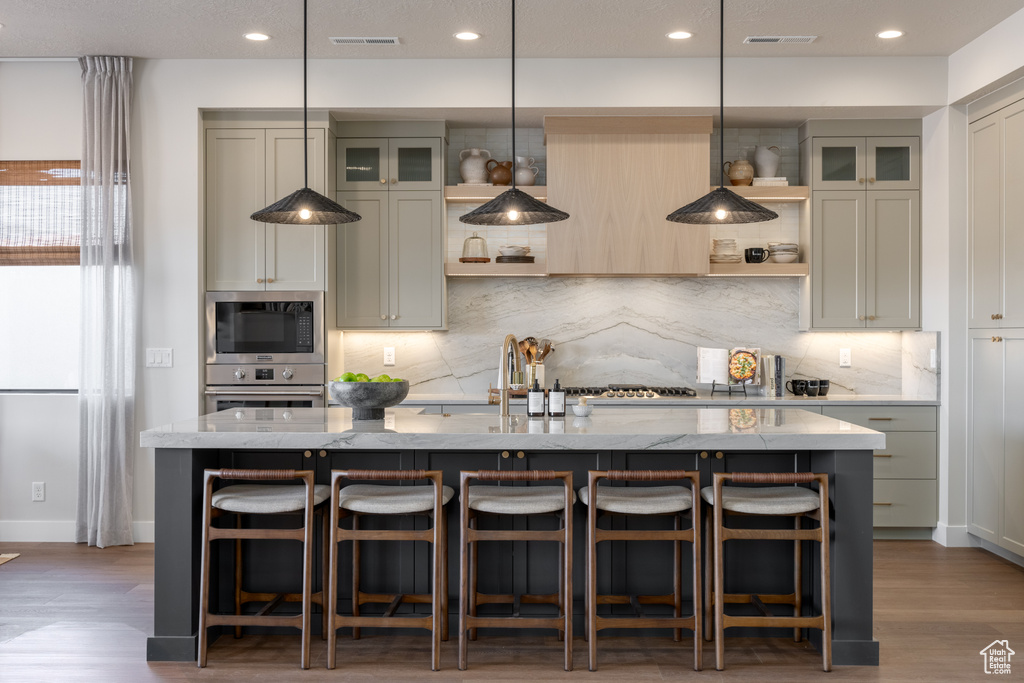 Kitchen with open shelves, appliances with stainless steel finishes, a kitchen island with sink, backsplash, and recessed lighting