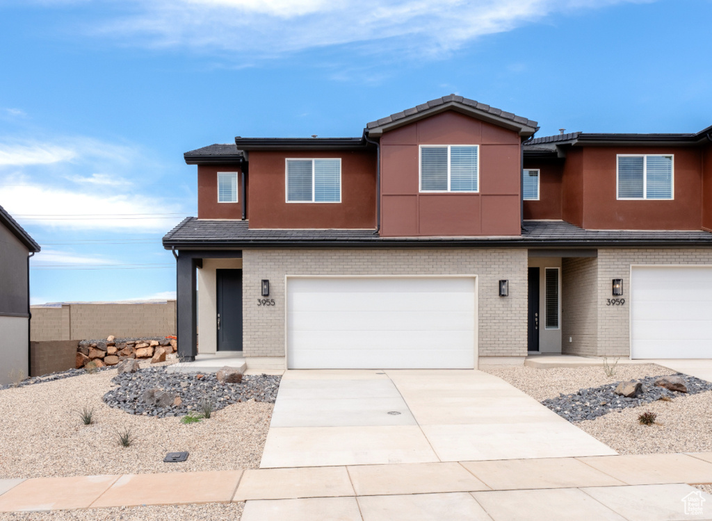 View of front facade with a garage, driveway, stucco siding, and brick siding