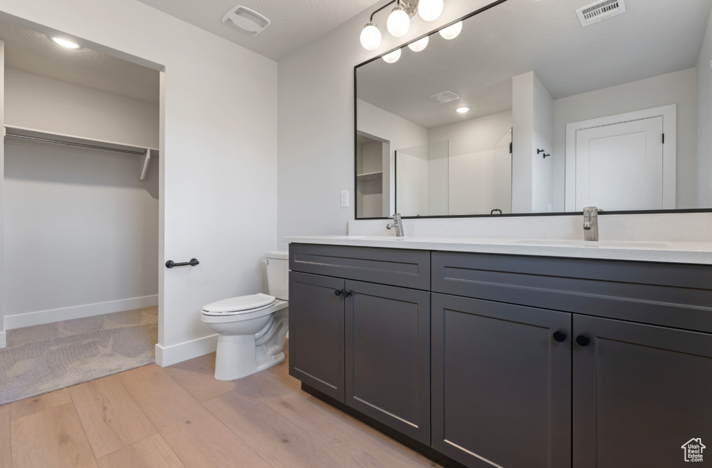 Bathroom featuring double vanity, wood finished floors, a spacious closet, and a shower